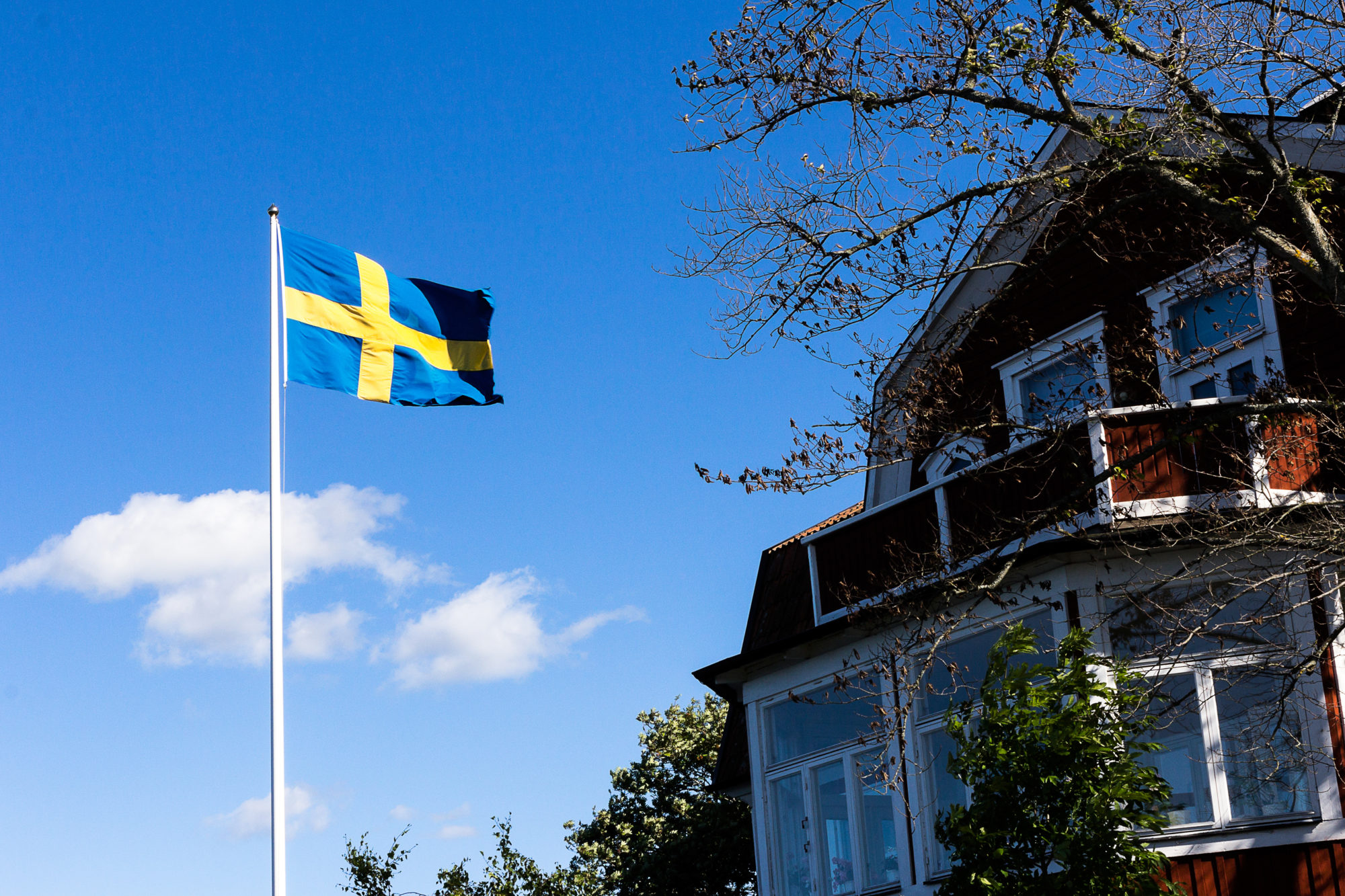 A swedish flag is wavering in the wind in front of a characteristic swedish home.